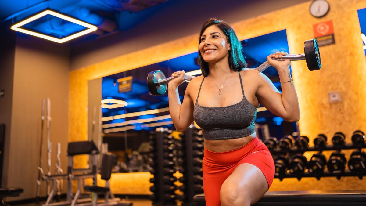 mujer con una pierna al frente con la rodilla flexionada y una barra z en la espalda sujeta con las dos manos, en posicion de sentadilla