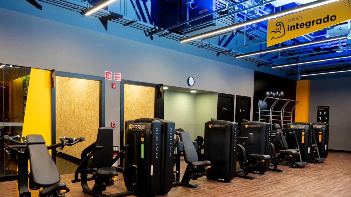 hilera de aparatos de peso integrado de un gimnasio smart fit, al fondo entrada a loss banos y area de estiramiento