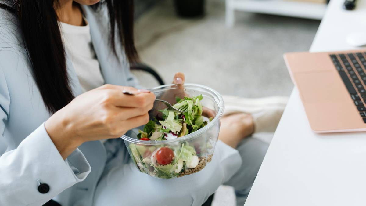 mujer sentada en una silla de oficina comiendo una ensalada de verduras