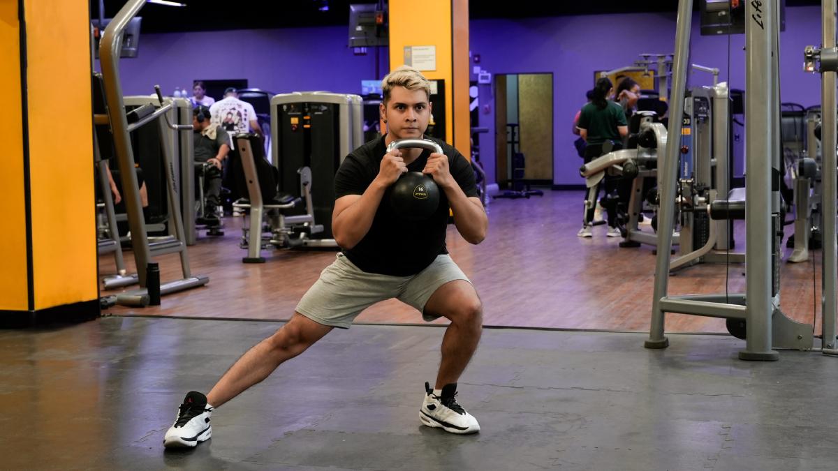 hombre realizando una sentadilla lateral con una pesa rusa. con una pierna flexionada y la otra estirada.