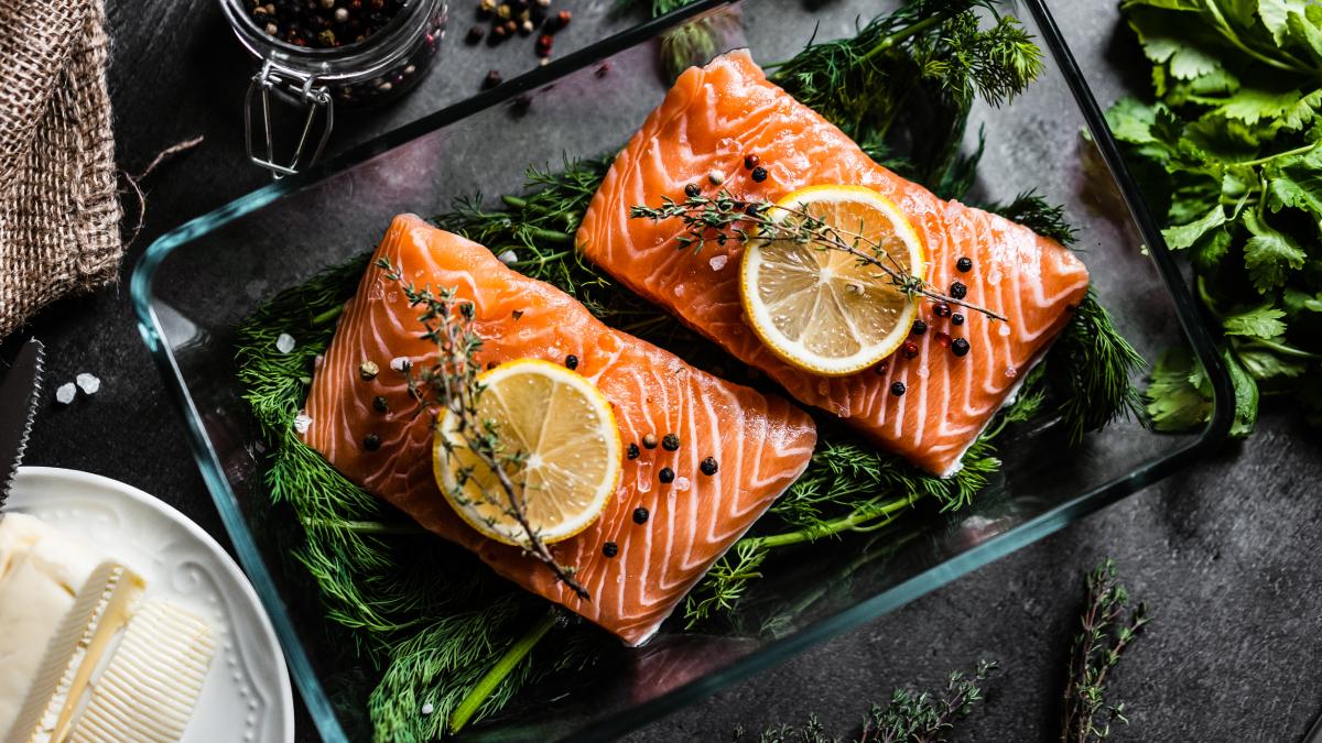 Dos trozos de salmón crudo con especies y un gajo de naranja, sobre un recipiente