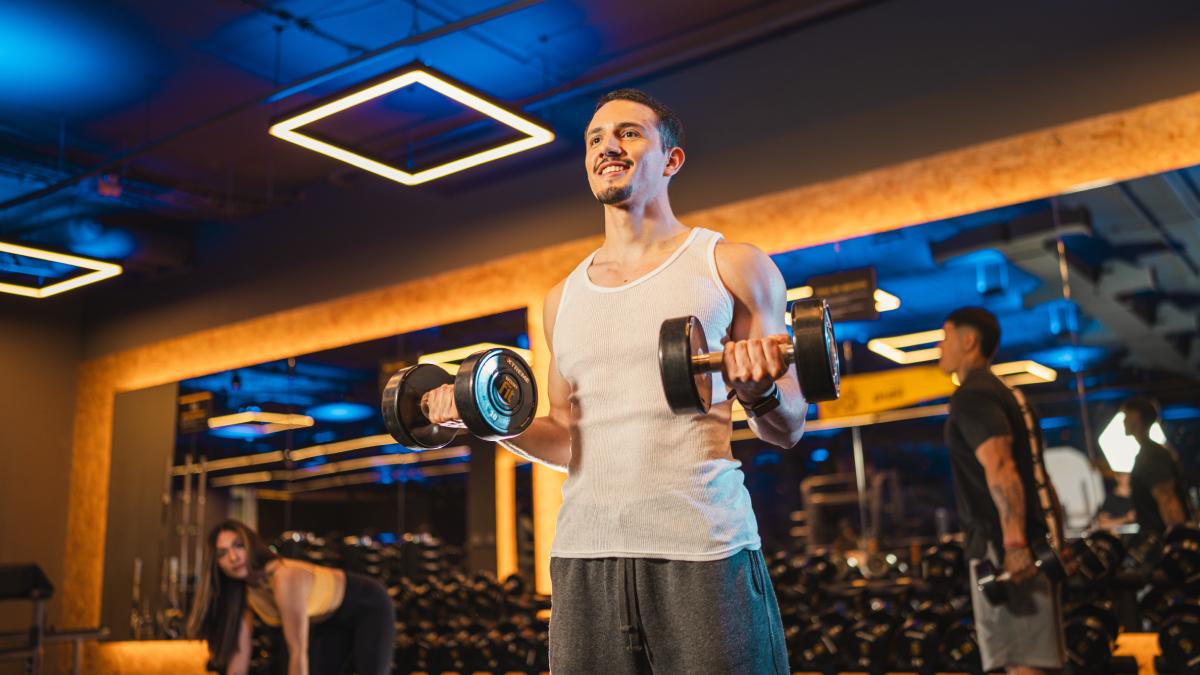 hombre de pie con una mancuerna en cada mano en posicion del ejercicio de curl de biceps