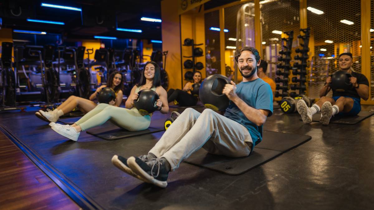 hombre sentado sobre el suelo de un gimnasio smart fit, realizando un giro ruso con una balon medicinal
