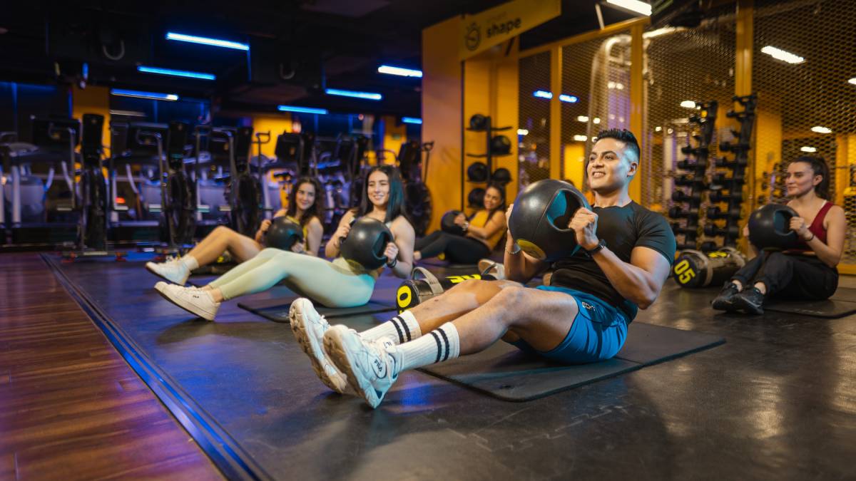 usuarios sentados sobre el suelo de un gimnasio smart fit, realizando un giro ruso con una balon medicinal