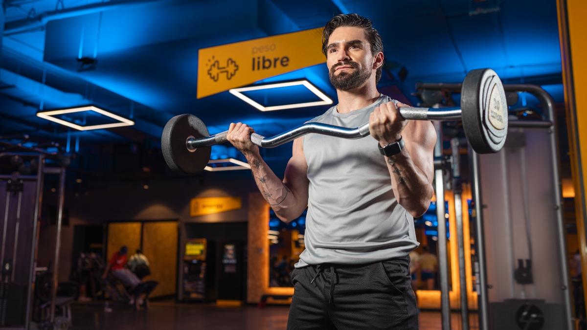 hombre parado en un gimnasio Smart Fit realizando un curl de biceps con una barra z
