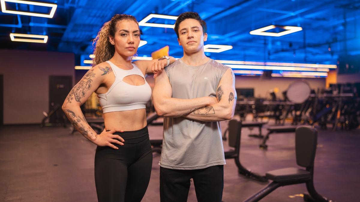 Dos personas en un gimnasio Smart Fit posando en un area de pesas, destacando la importancia de la recuperacion muscular en un entorno fitness profesional
