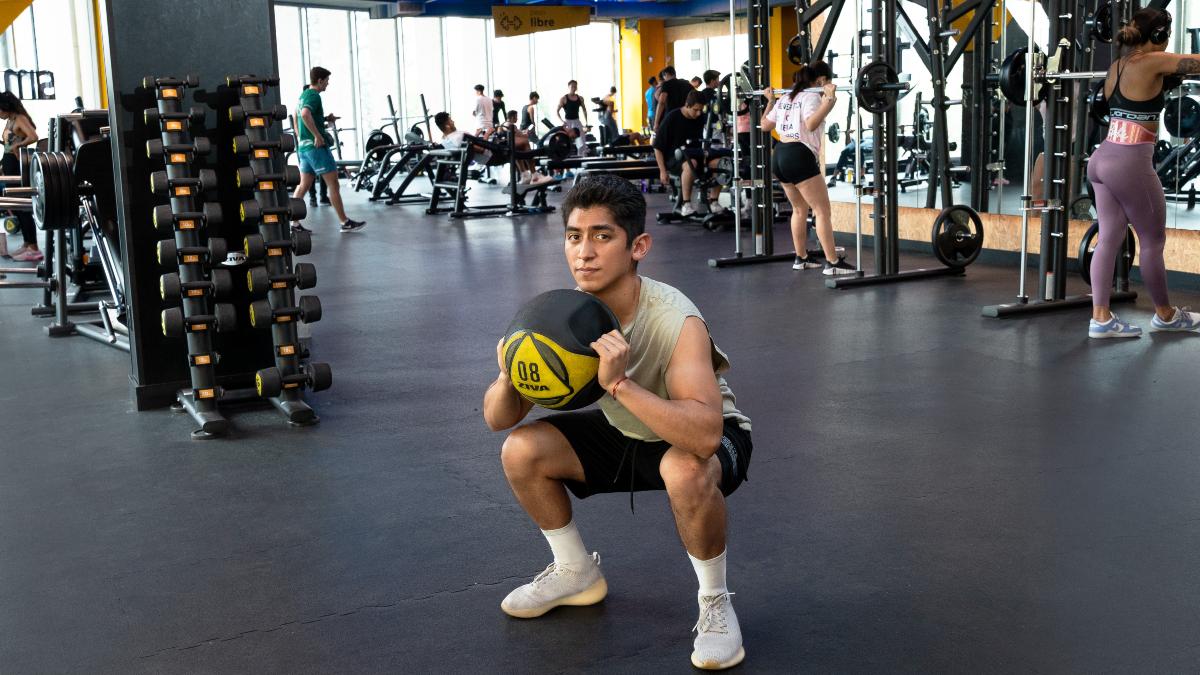 Persona realizando sentadillas con balon medicinal como parte de un entrenamiento funcional en los gimnasios Smart Fit, rodeado de un ambiente moderno y activo.