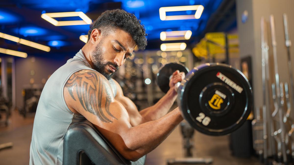 Hombre realizando curl de biceps en gimnasios Smart Fit, destacando la importancia de hacer ejercicio en invierno para mantenerse activo y alcanzar metas fitness.